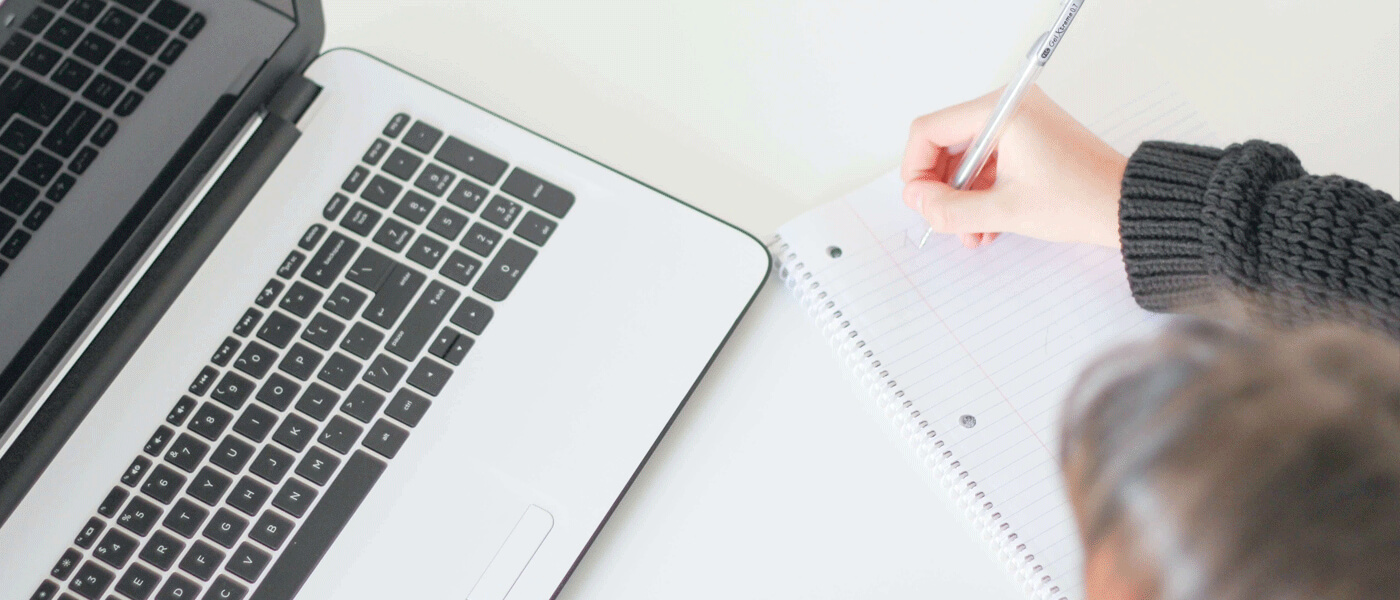 Person making notes on pen and paper while using laptop