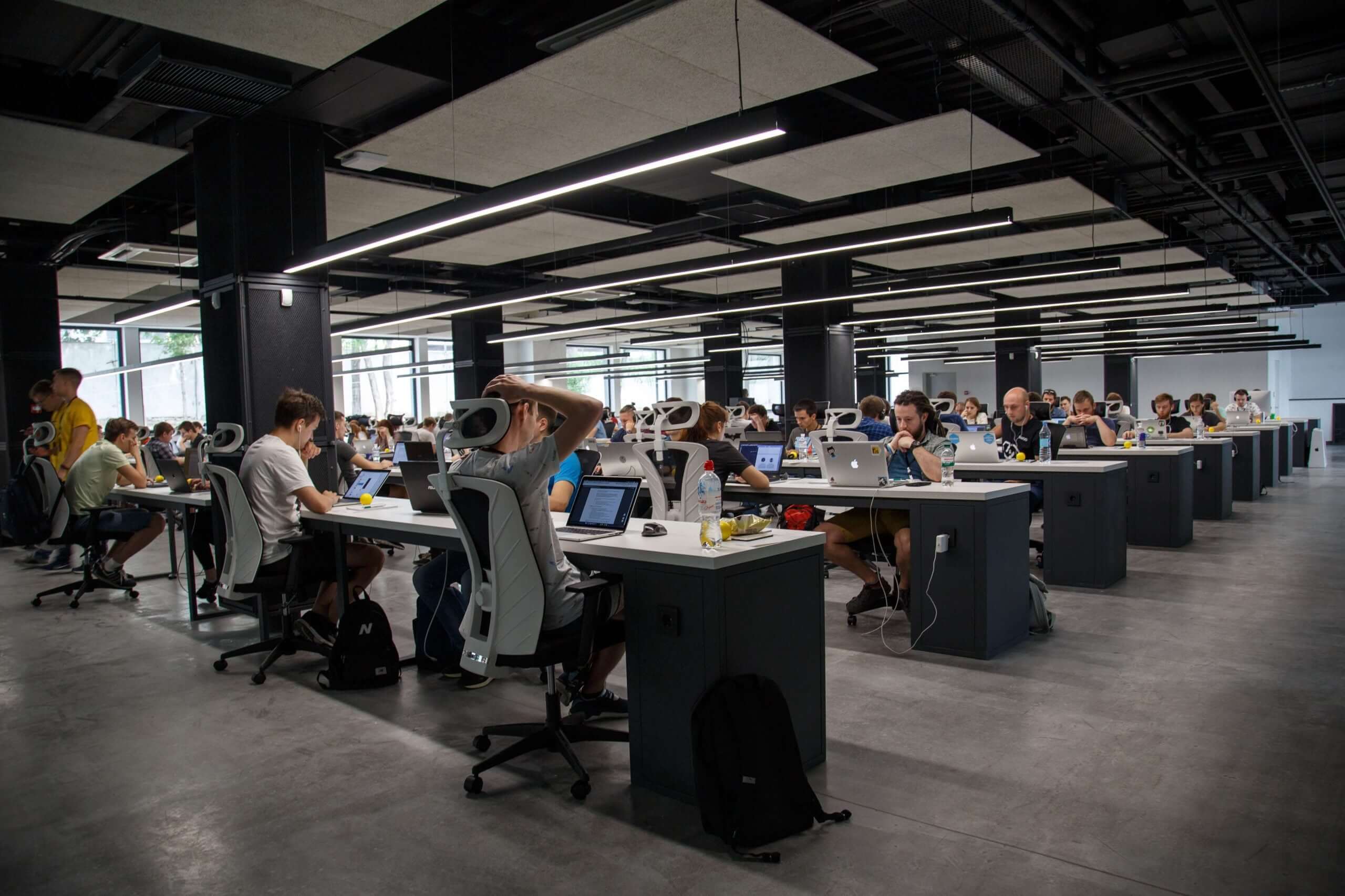 A large, industrial open plan working space full of people at desks working on laptops.