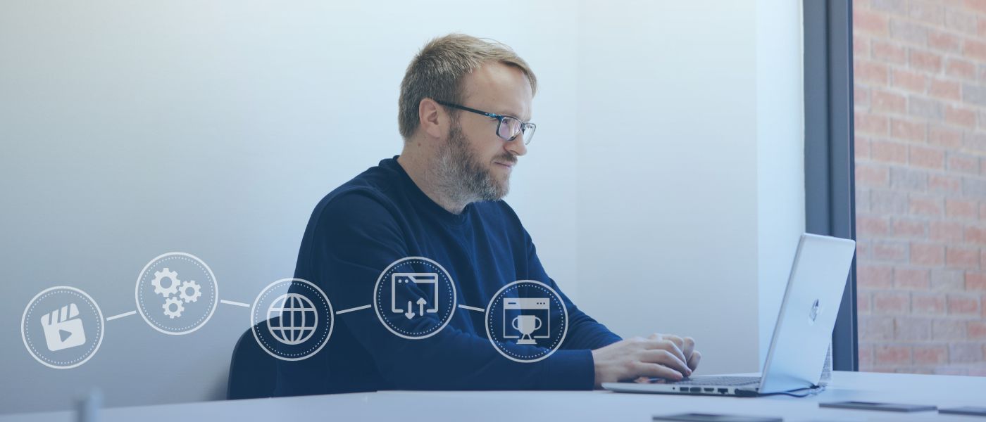 A man working at a desk with a laptop displaying various icons on the screen.